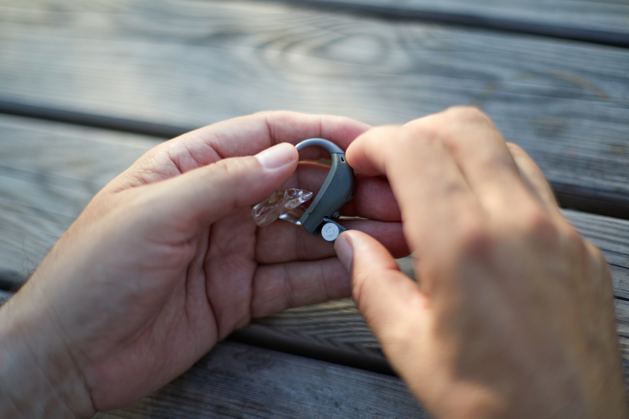 Close up of a person holding a hearing aid at a table.