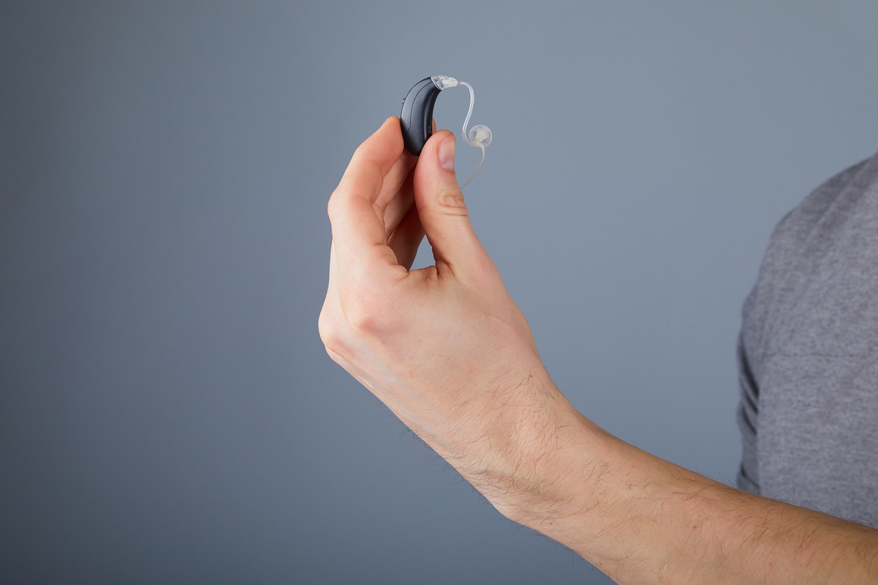 Man holding up a hearing aid against a grey background